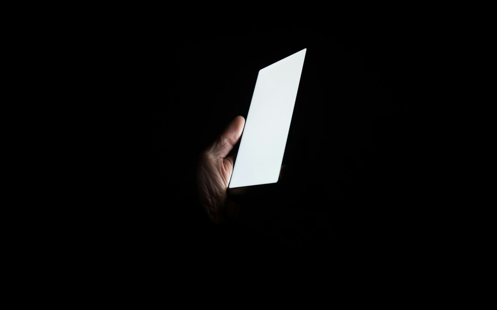 Main tenant un téléphone allumé dans l'obscurité